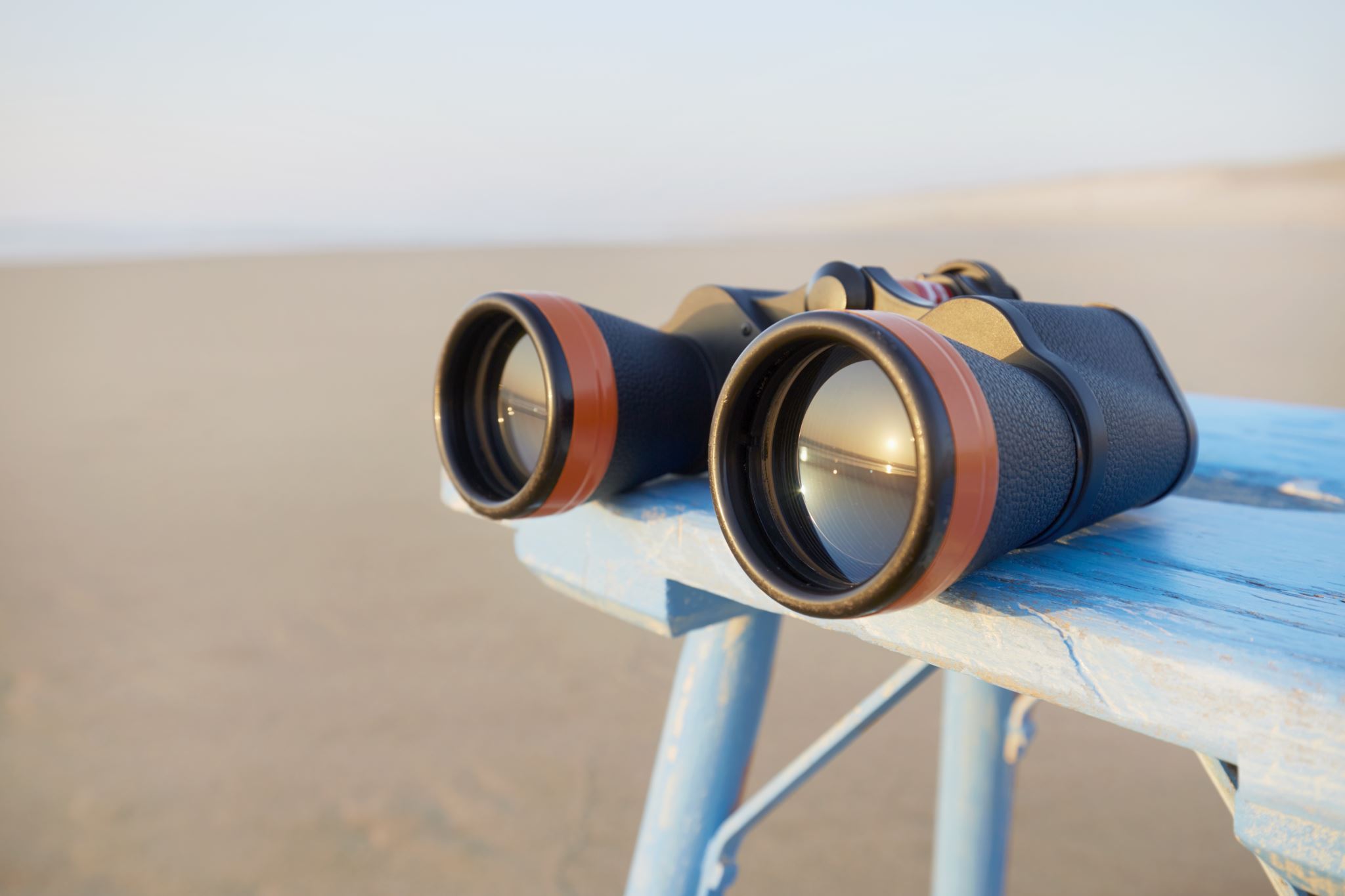 Binoculars-reflecting-a-sunset-and-laying-on-table-by-the-sea